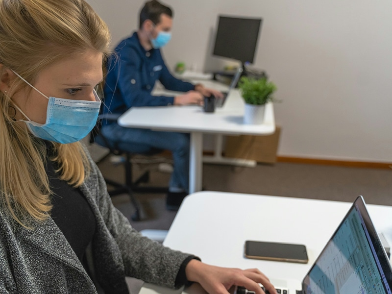 Two colleagues work at desks 2m apart whilst wearing covid-19 masks