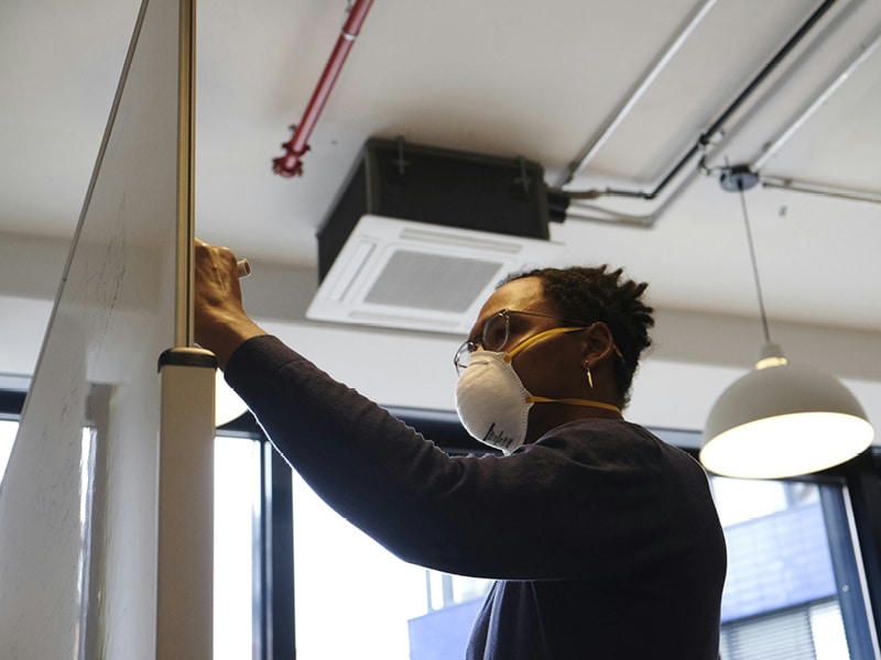 A man wearing a dust mask works on a whiteboard