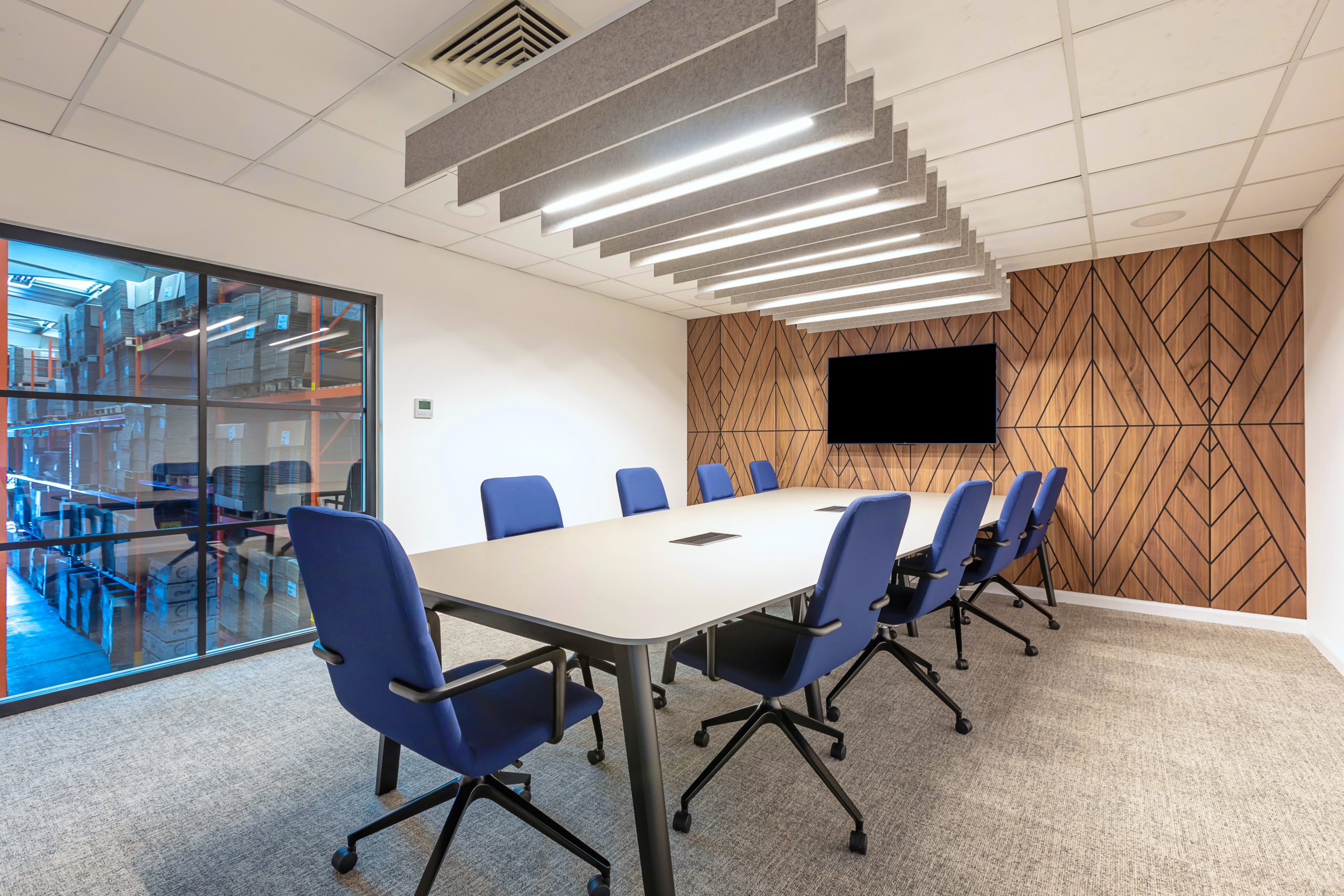 Boardroom with blue chairs and tv overlooking warehouse through glass