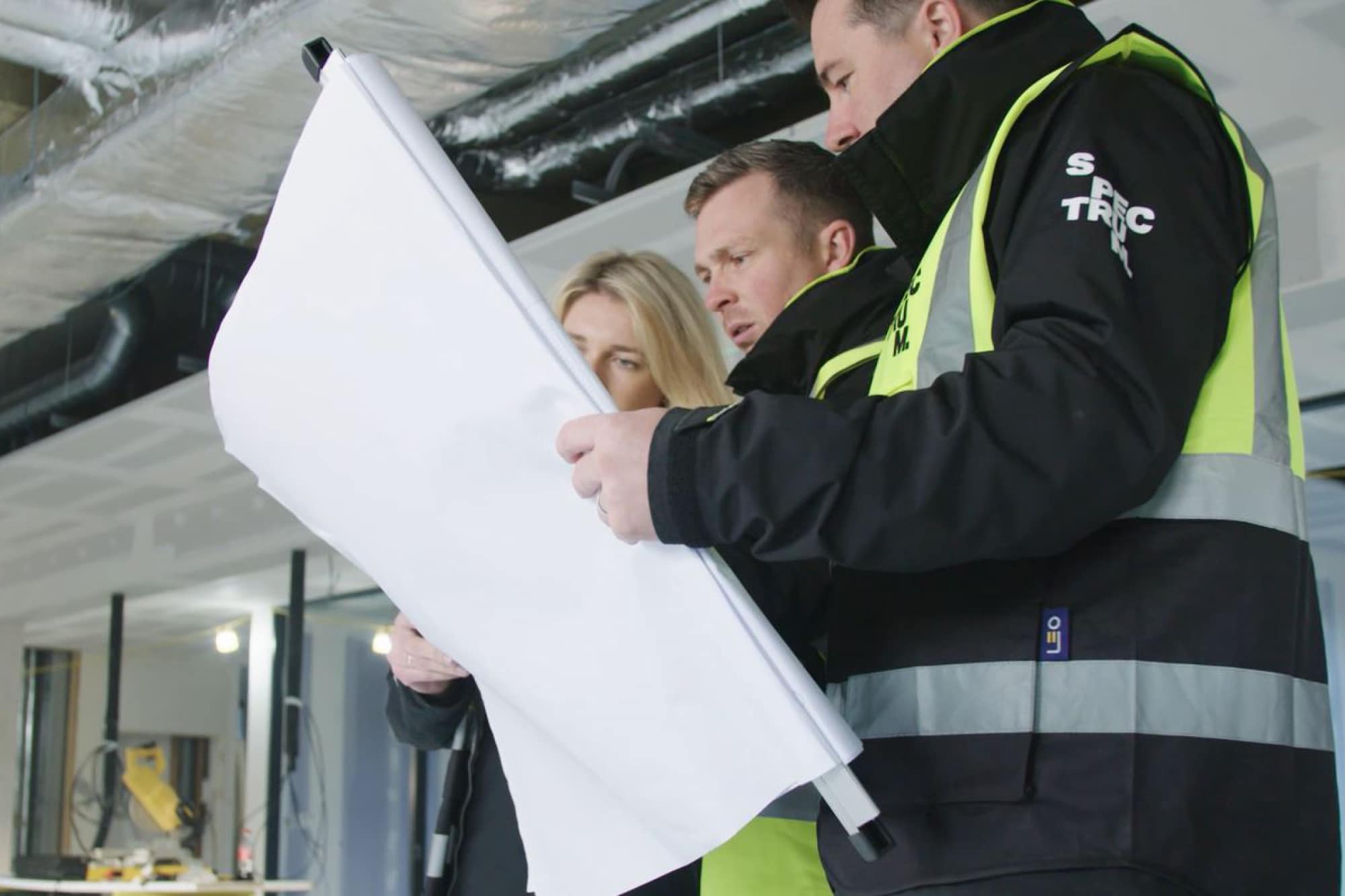 Three people look at plans for a workplace whilst on site