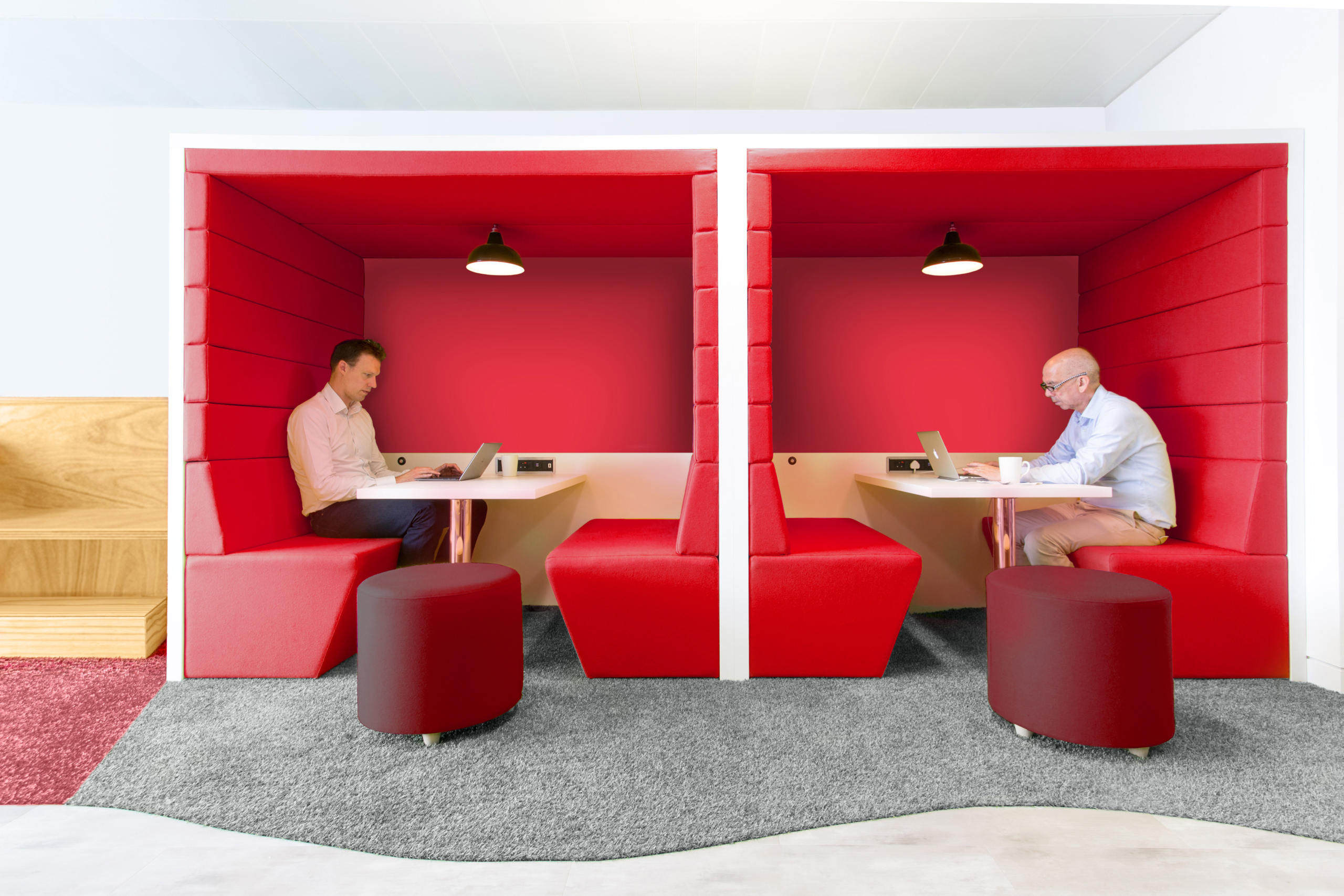 Red booth seating with two men sitting in it working on laptops